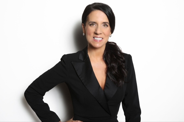 Ann Marie Klotz, a light-skinned woman with dark hair in a low ponytail over her shoulder, smiles for a headshot in a black blazer