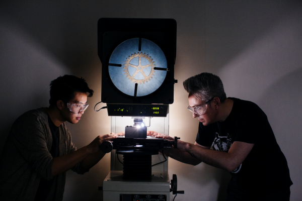 Two students line up a gear under a microscope.