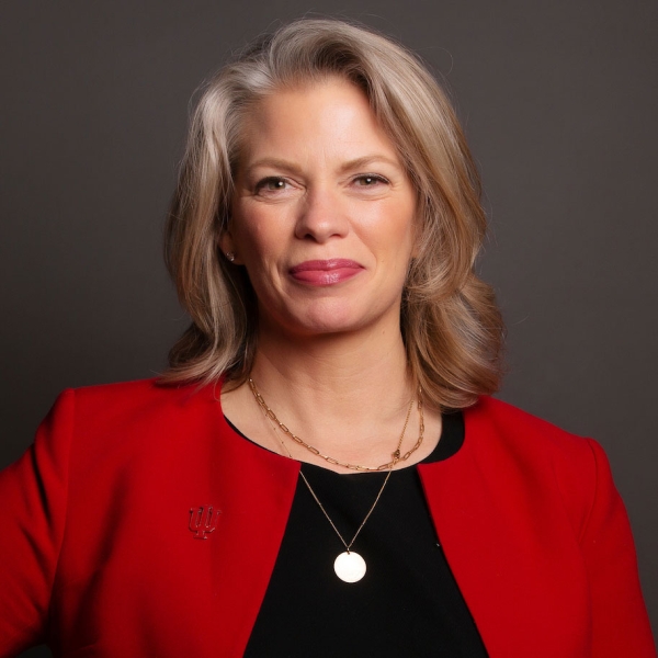 Julie Payne-Kirchmeier, a light-skinned woman with shoulder-length blond hair, smiles for a head shot wearing a black blouse and red blazer