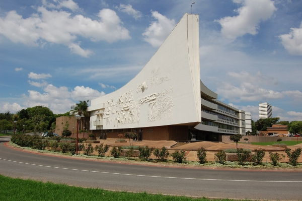 A white building that looks like a ship set against a bule sky with clouds. In front of the building, there is a road.