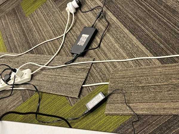 A mess of laptop charging cords on a brown rug.