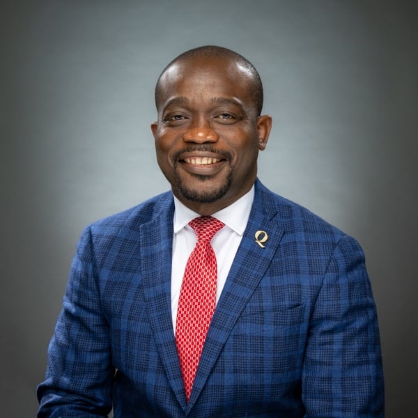 Kafui Kouakou poses for a headshot wearing a blue suit, red tie and Q pin on his lapel.