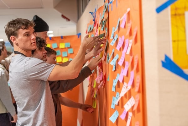 A student applies sticky notes to a hallway at Bryant University during IDEA