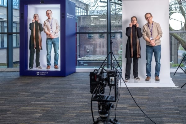 A man and a woman on the right are being recorded by a camera in the foreground, and their 3-D images are displayed in a person-size blue box on the left