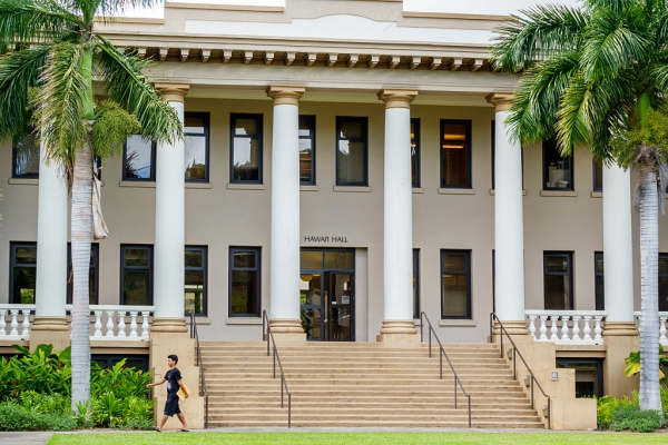 A large white building with multiple pillars is framed by palm trees 