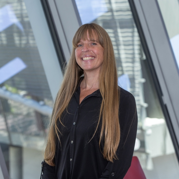 Patty Goedl smiles in a window-lit room, wearing a black button-up shirt