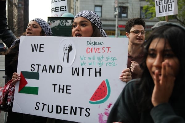 A woman holding a sign that says, "We stand with the students."