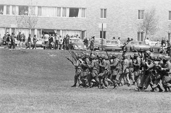 a black and white image of armed soldiers marching across Kent State University's campus