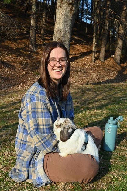 A student sits on Warren Wilson's campus with a white and brown rabbit on their leg