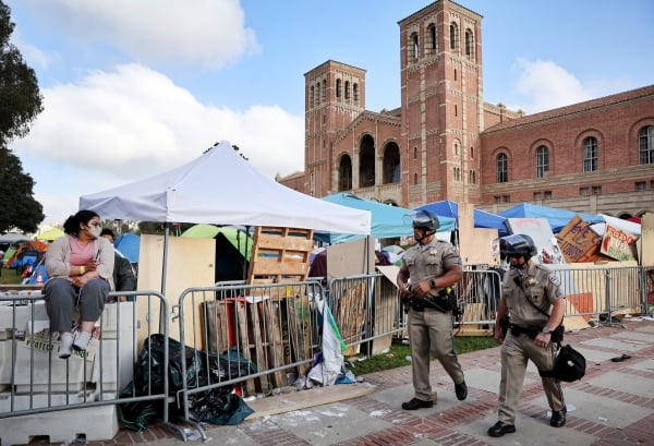 Police patrol a barricade in front of tents on UCLA campus