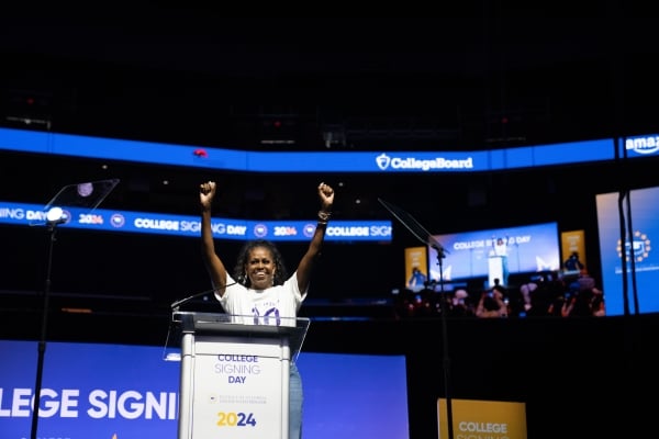A woman raises her hands in front of a podium on a stage