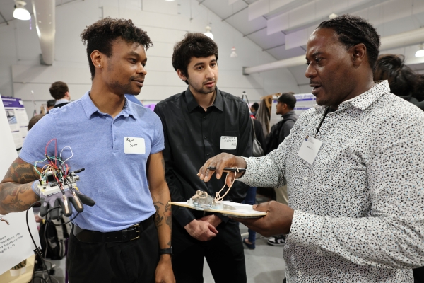 Two students demonstrate a robotic hand they designed to a faculty judge at a research symposium
