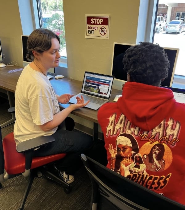 Two students sit in a computer lab working on their laptops.