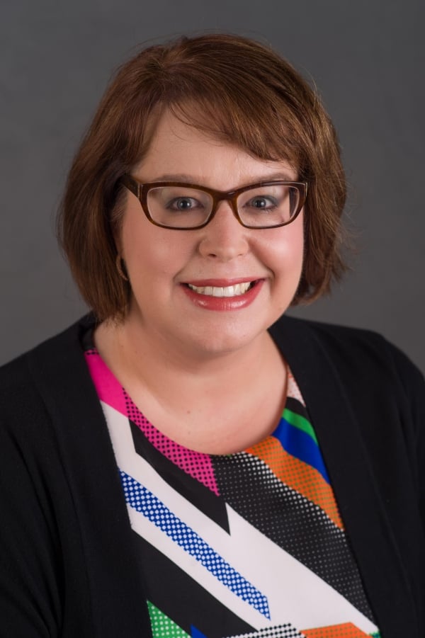 Jennifer Lasater smiles for a headshot wearing a black blazer and multicolor blouse