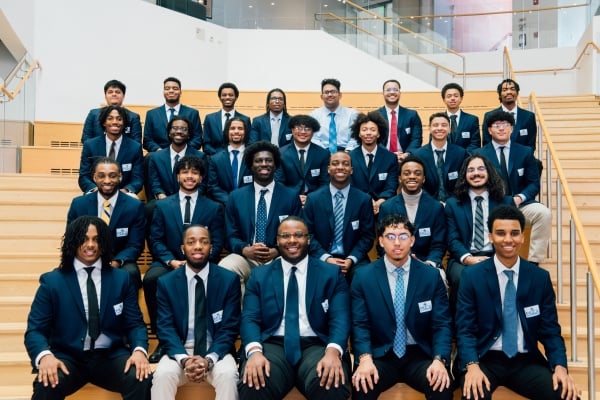 A group of young men smile in business professional clothing on a stairwell.