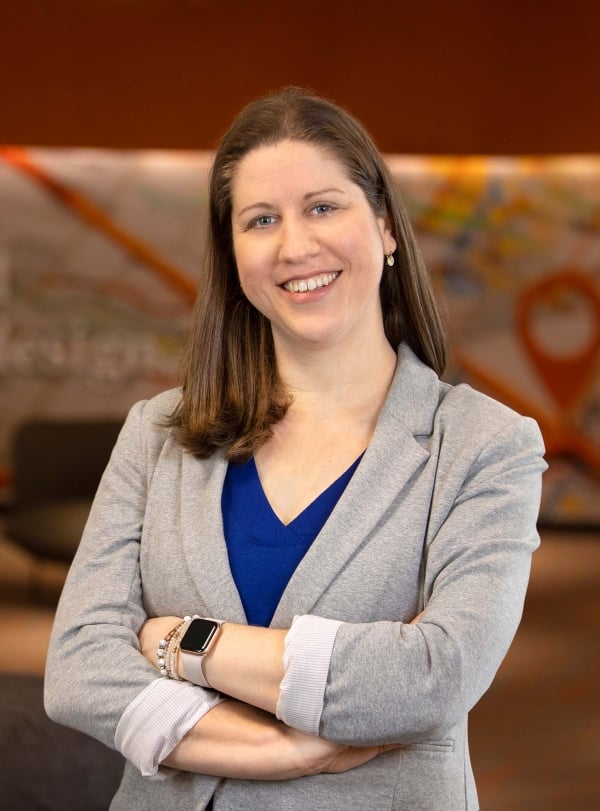 Adrienne Ausdenmoore smiles for a headshot wearing a gray suit coat and a blue shirt