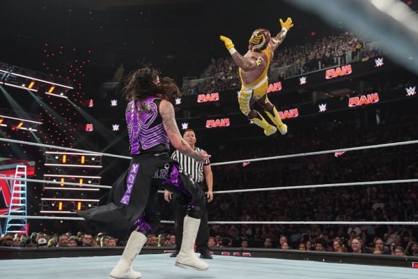 A wrestler in yellow jumps toward a wrestler in purple.