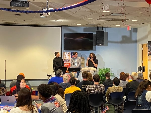 Three speakers sit on a stage with audience members facing them