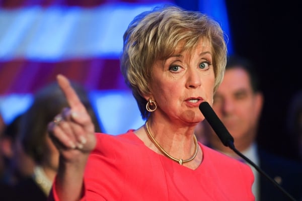 Linda McMahon, wearing a pink blouse, gestures before a microphone