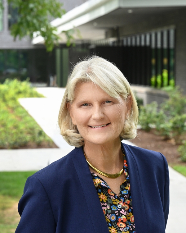 Portrait of Elizabeth Bradley, a white woman with blond hair wearing a blue blazer over a flower-patterned blouse