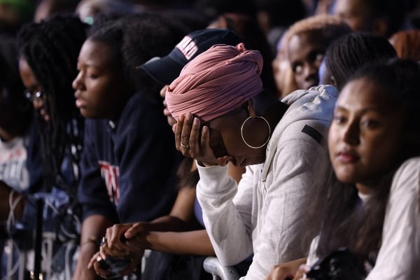 a woman wearing a pink head wrap and large hoop earrings puts her hand on her head outside at Howard University