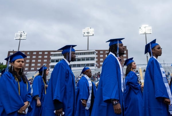 Four Tennessee State University students walk in blue caps and gowns.