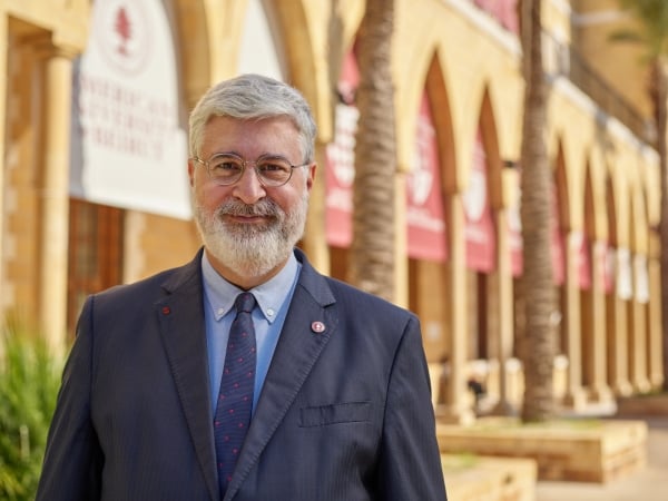 Dr. Khuri, a light-skinned man with white hair and a beard, wearing glasses and a blue suit with a blue shirt and tie.