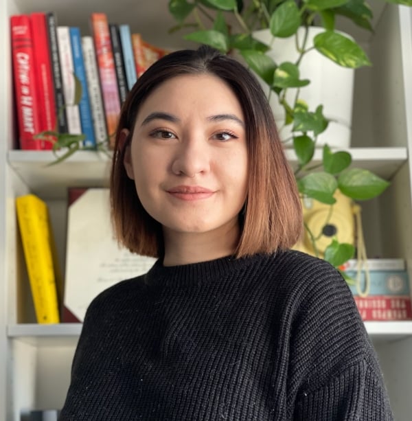 A woman with a brown bob poses in front of a bookshelf
