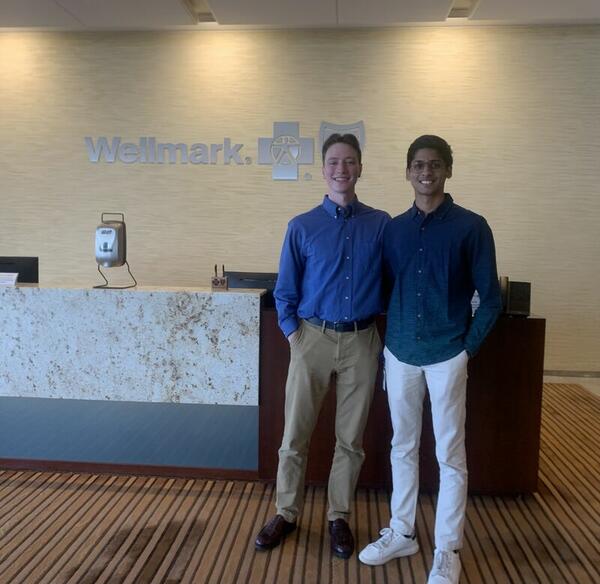 Two men pose for a photo in an office building with the sign Wellmark behind them. 