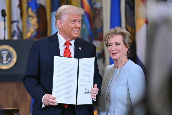President Trump stands next to Linda McMahon while holding up an executive order with his signature.