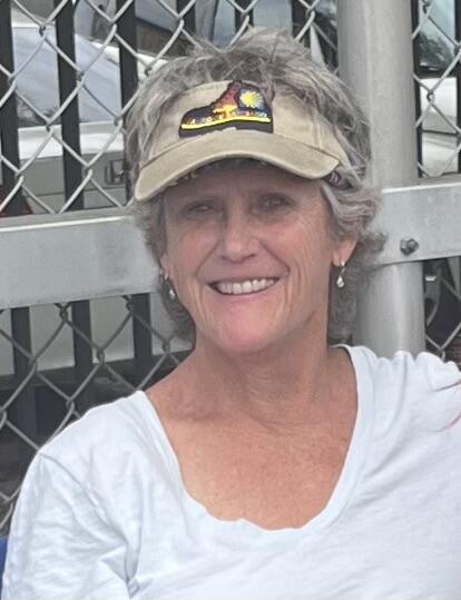 Katherine Taylor smiles for a headshot outside wearing a white blouse and a tan visor