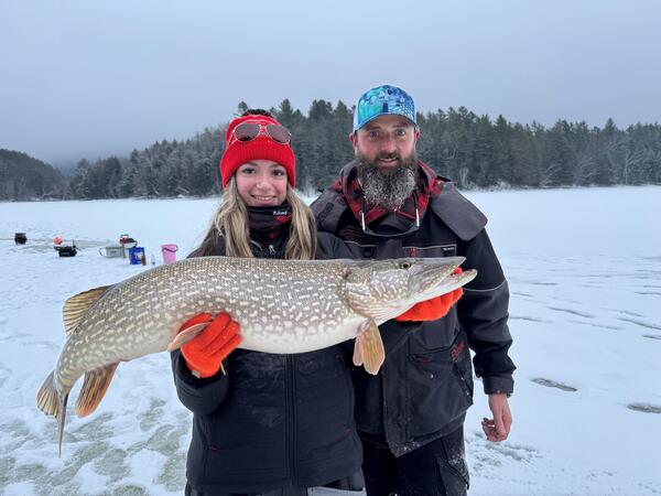 Two people stand outside in the snow, one holding a large fish. It's a really large fish.