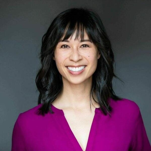 Christine Cruzvergara smiles for a headshot against a gray backdrop wearing a purple v-neck blouse.