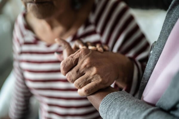 A close-up photo of a caregiver holding the hand of an elderly patient.