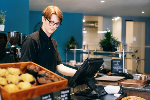 A photo of a young man working the cash register at a coffee shop.