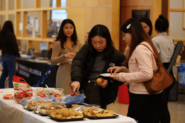 A group of students eat snacks off a table with a white tablecloth and cookies and apples.