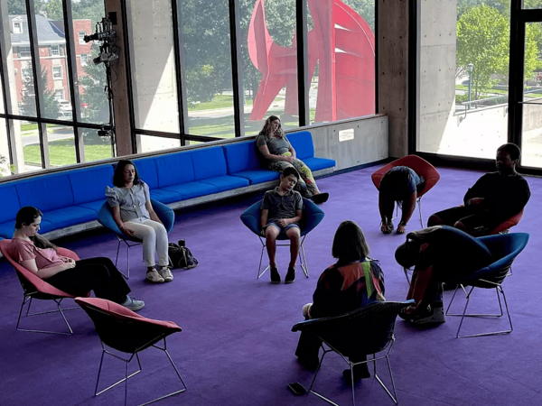 Six students sit in chairs with their eyes closed in relaxed postures as they meditate.