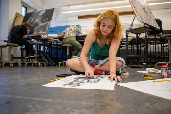 A student draws with charcoal on the floor of a visual arts studio