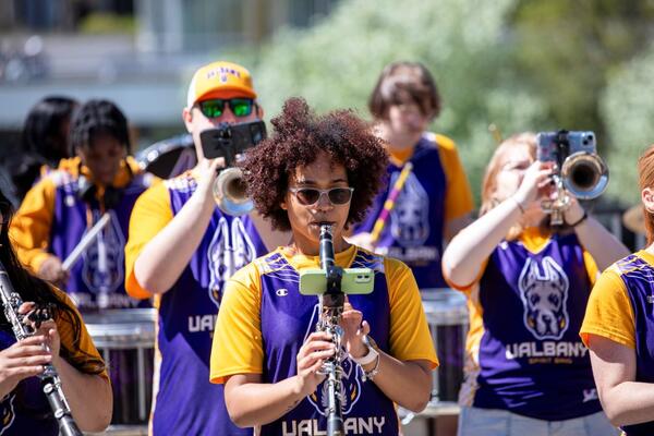 Band members at the University at Albany perform outside, wearing sunglasses and UAlbany sports jerseys