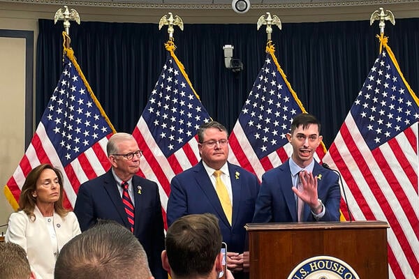 A photo of speakers at Tuesday’s Capitol Hill press conference standing in front of several American flags.