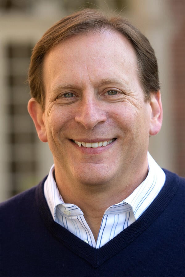 Headshot of Phillip Levine, a light-skinned man with brown hair wearing a blue pullover sweater over a striped collared shirt.