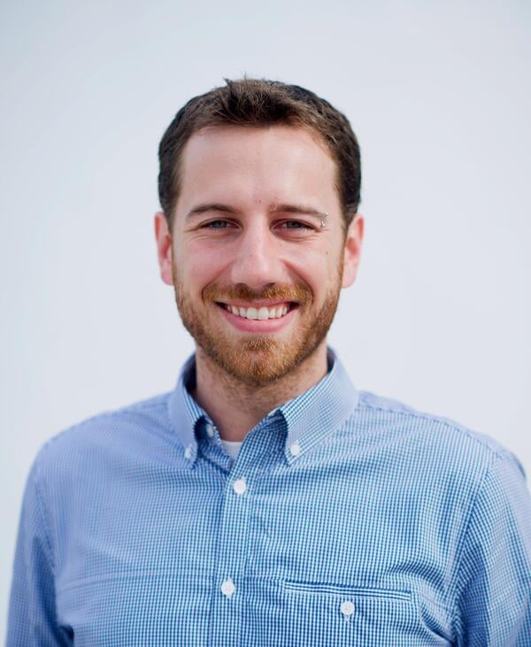 Headshot of a light-skinned man with brown hair and a short beard, wearing a blue button-down shirt.