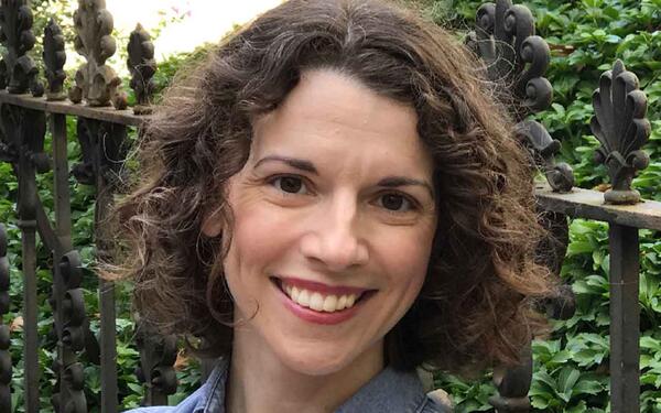 A light-skinned woman with curly brown hair parted in the middle