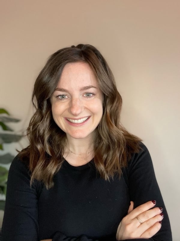 Julia Dallos, a light-skinned woman with wavy brown hair longer than shoulder length, wearing a black crew-neck top.