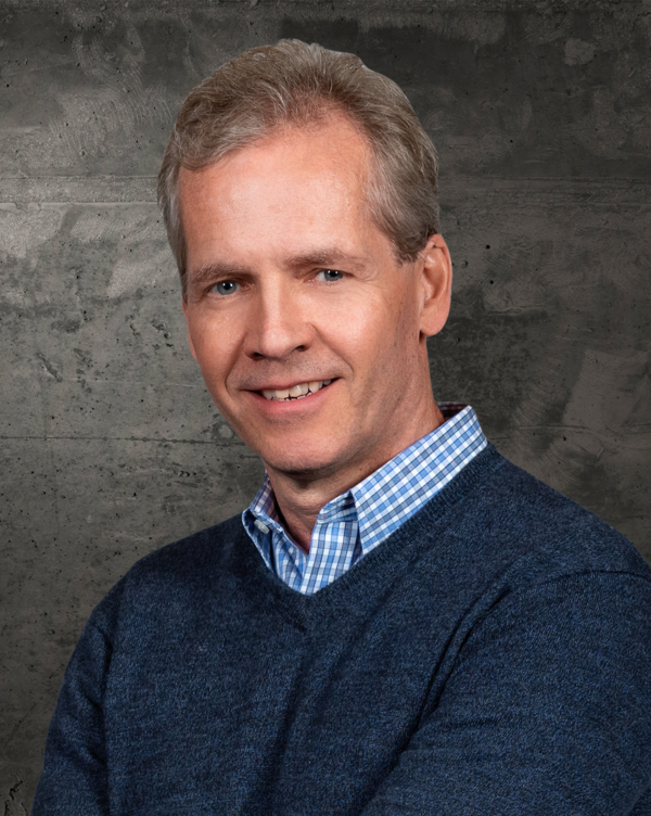 Kees Bol, a light-skinned man with gray hair wearing a blue sweater over a blue-checked collared shirt.
