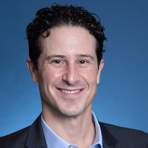 Nick LaRusso, a light-skinned man with short, curly dark hair, wearing a blue collared shirt under a dark jacket.