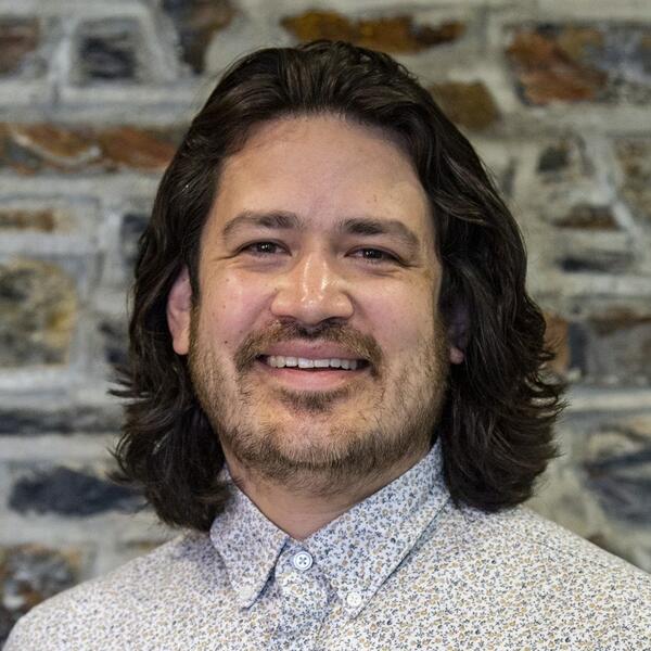 Quentin Ruiz-Esparza, a man with light skin, shoulder-length dark hair, and stubble.