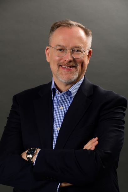 Scott Jeffe, a light-skinned man with a goatee and glasses wearing a blue-checked collared shirt and a dark blazer.