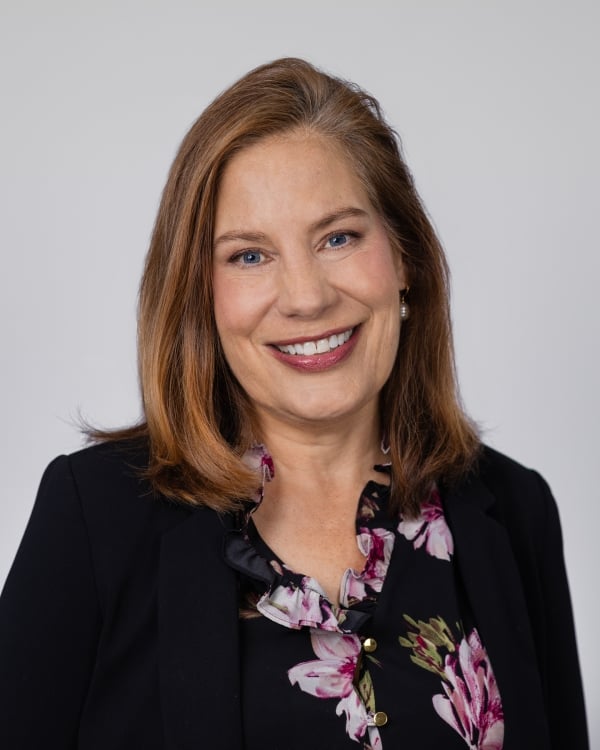 Anne Trumbore, a light-skinned woman with shoulder-length hair wearing a flowered black top.