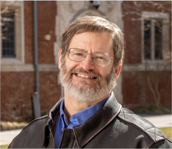 Charles Bailyn, a light-skinned man with light-brown hair and a bear with some gray. He is wearing glasses and a blue collared shirt under a brown leather jacket.